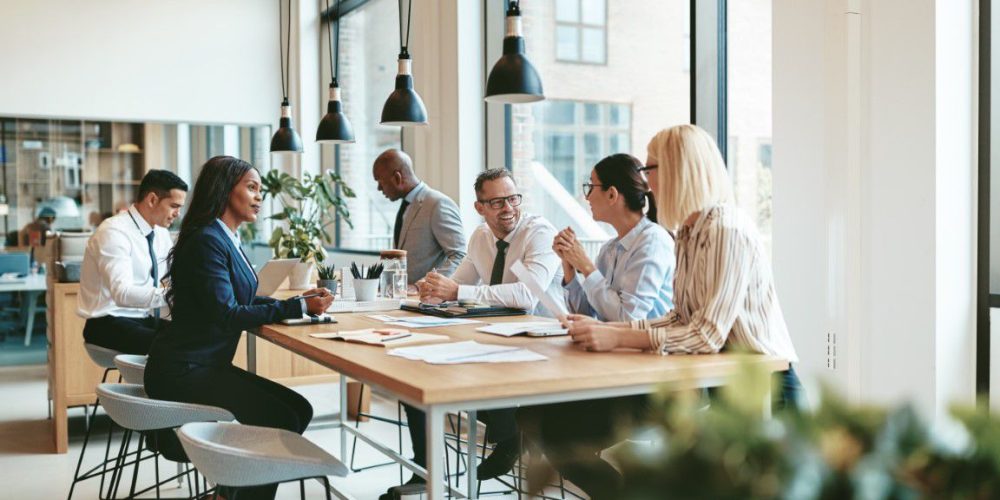 Smiling group of diverse businesspeople discussing paperwork together while having a meeting around a table in a modern office