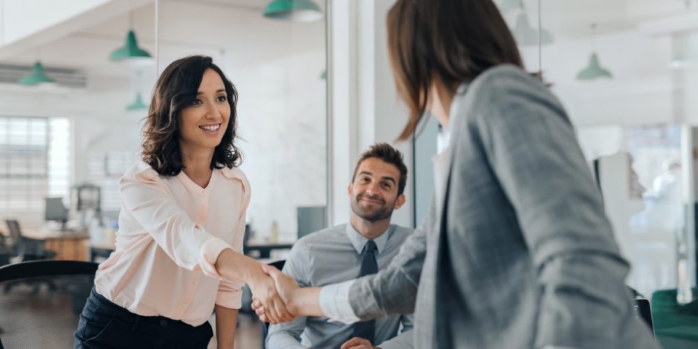 Smiling young businesswoman shaking hands with a coworker during a meeting with colleagues around a table in an office boardroom